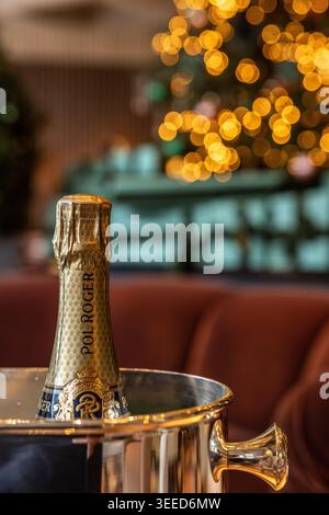 Une bouteille de champagne Pol Roger fraîche dans un seau à glace argenté, sur un fond chaleureux et festif avec des lumières de sapin de Noël éclatantes. Banque D'Images