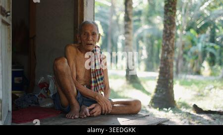 Homme âgé reposant sur un porche en bois, regardant la caméra, mode de vie rural Banque D'Images