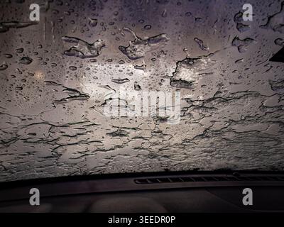 Vue abstraite de fortes pluies et de feuilles d'eau coulant à travers un pare-brise de voiture de la perspective intérieure avec un éclairage et des textures gris d'humeur sombre Banque D'Images