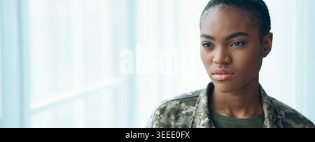 Jeune femme en uniforme militaire semble réfléchie dans un cadre intérieur lumineux Banque D'Images