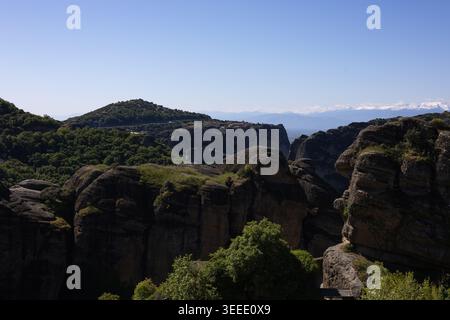 vue panoramique sur les anciens monastères perchés au sommet des piliers rocheux de grès imposants dans les météores, grèce, sous un ciel bleu clair avec m enneigé lointain Banque D'Images