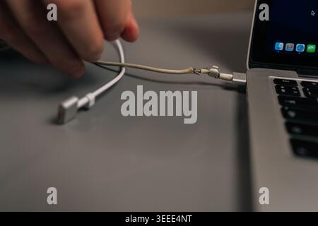 Personne tenant un câble de chargeur d'ordinateur portable endommagé avec des fils exposés, illustrant une défaillance de l'appareil électronique et le danger potentiel d'usure électrique Banque D'Images