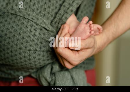 Père aimant tenant les pieds minuscules des nouveau-nés dans le porte-bébé Banque D'Images