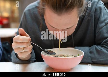 Homme savourant un bol de nouilles dans un restaurant asiatique confortable. Guy appréciant la nourriture de confort chaud avec une expression satisfaite dans un restaurant décontracté. Ambiance décontractée du bar à nouilles avec délicieux repas Banque D'Images