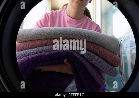 Femme chargeant des serviettes propres colorées dans la machine à laver à la maison, la routine domestique de jour de lessive vue rapprochée du sèche-linge Banque D'Images