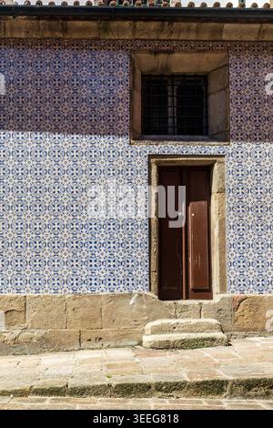 Façade traditionnelle portugaise entièrement recouverte de carreaux de céramique azulejo bleus et blancs avec une porte en bois et une fenêtre barrée sur des marches en pierre. Banque D'Images