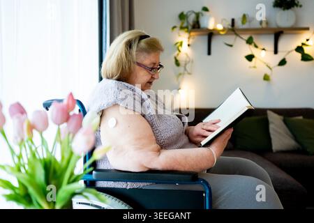 Femme âgée avec moniteur de glucose continu appréciant le temps calme à la maison. Banque D'Images