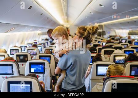 Maman calmant l'enfant bouleversé pendant le vol familial en voyageant dans l'avion. Banque D'Images