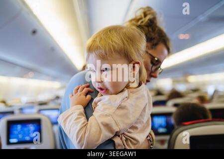 Maman calmant l'enfant bouleversé pendant le vol familial en voyageant dans l'avion. Banque D'Images