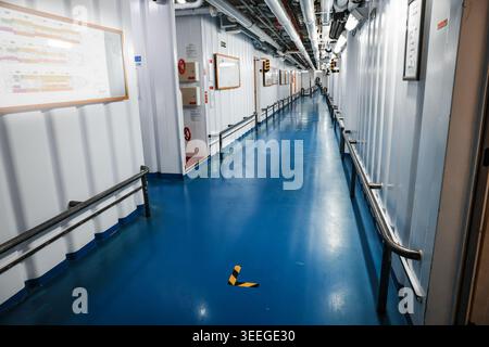 long couloir intérieur industriel et passerelle réservée à l'équipage à bord d'un navire de croisière avec des murs blancs, un sol bleu et des tuyaux aériens Banque D'Images