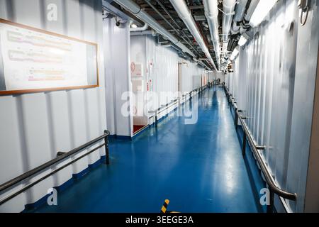 long couloir intérieur industriel et passerelle réservée à l'équipage à bord d'un navire de croisière avec des murs blancs, un sol bleu et des tuyaux aériens Banque D'Images