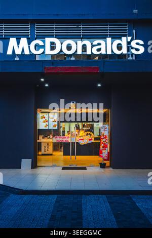 Une vue nocturne de l'entrée d'un restaurant McDonald's avec un panneau lumineux lumineux, des portes vitrées et du personnel. Banque D'Images