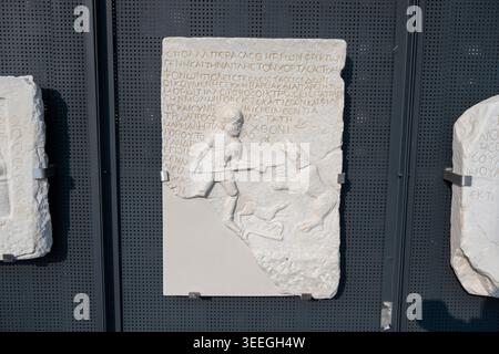 Veria, Grèce - 16 août 24 : fragment de marbre grec ancien d'un jeune avec lance et chien sous l'inscription grecque au Musée archéologique o Banque D'Images