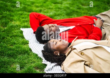 Couple afro-américain se relaxant sur l'herbe dans le parc profitant de moments paisibles loin de la ville bruyante. Banque D'Images