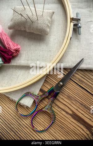 Outils et matériaux de broderie sur fond de bois : cerceau de broderie avec tissu de lin, fils colorés, coussin d'aiguille et ciseaux décoratifs. Besoin Banque D'Images