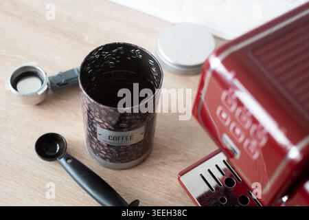 Gros plan d'un récipient décoratif à grains de café à côté d'une machine à espresso rouge et d'une tasse à café blanche sur un comptoir de cuisine avec lumière naturelle et shal Banque D'Images