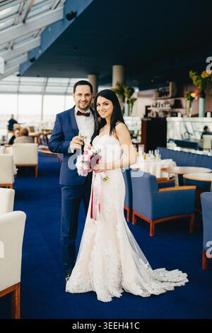 Portrait vertical de la belle mariée et mariée femelle tiennent des verres avec du champagne, célèbrent leur occasion spéciale, ont des expressions heureuses, regardent directement dans la caméra. Concept de célébration Banque D'Images