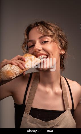 Jeune femme boulangère souriante et profitant de baguette fraîche, représentant la boulangerie et l'artisanat traditionnel du pain Banque D'Images