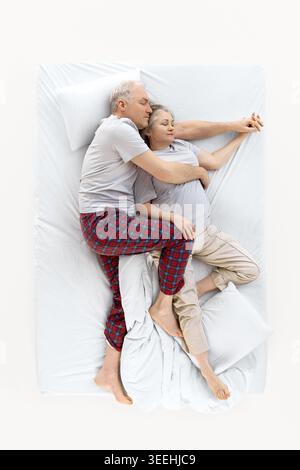 Homme plus âgé embrassant la femme tout en dormant sur un lit blanc d'en haut. Banque D'Images