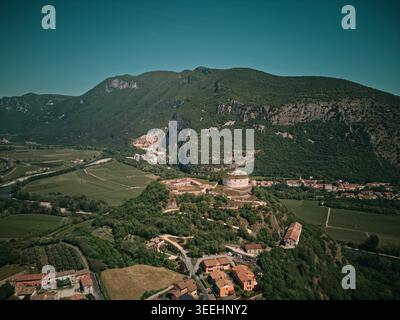 Vue aérienne d'une forteresse historique en pierre sur une colline verdoyante surplombant les vignobles et une vallée sinueuse de la rivière avec des montagnes en arrière-plan Italie. Banque D'Images