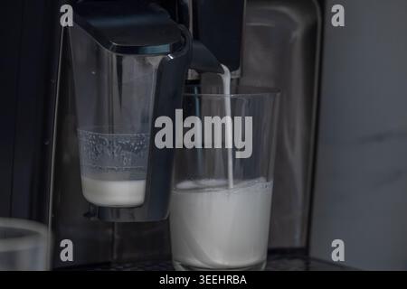 Machine à espresso automatique versant du lait chaud dans le verre pendant la préparation du café dans un cadre moderne de cuisine. Barista à domicile et café de spécialité Banque D'Images