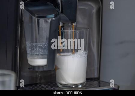 Machine à espresso automatique versant le café dans le lait chaud pendant la préparation du latte ou du cappuccino dans la cuisine moderne. Barista à domicile et spécialité Banque D'Images