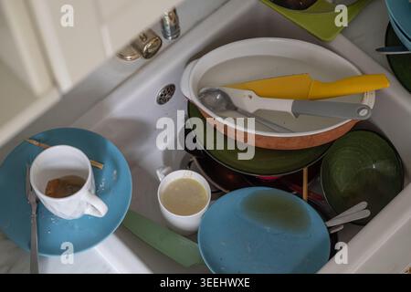 Vaisselle sale, tasses et ustensiles de cuisine empilés dans l'évier de cuisine après un repas de famille quotidien dans un environnement domestique réaliste. Style de vie domestique authentique et ho Banque D'Images