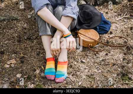 La personne est assise sur le sol de la forêt portant des chaussettes arc-en-ciel et un bracelet. Expression de l'identité de genre, représentation LGBTQ dans les médias, vie queer authentique. Banque D'Images