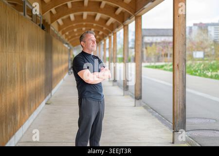 Portrait complet du corps d'un homme d'affaires mature confiant debout avec les bras croisés dans un environnement architectural en bois moderne. Style de vie professionnel, Banque D'Images