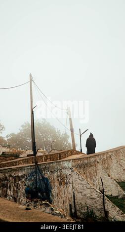 Larache, Maroc - mai, 04, 2026 : silhouette solitaire marchant à travers un village marocain brumeux avec des murs anciens et des poteaux utilitaires dans un atmo mystérieux Banque D'Images
