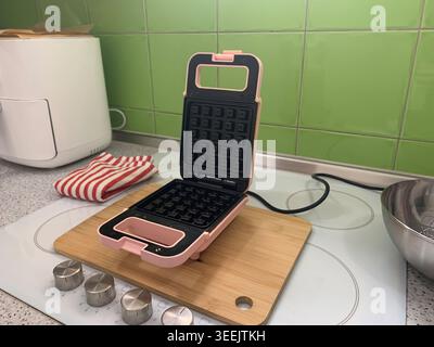 Vue de droite à angle élevé d'une gaufrière rose ouverte et d'un appareil blanc sur un comptoir de cuisine. Banque D'Images