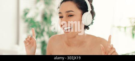 Femme aime la musique tout en portant des écouteurs et en souriant dans un cadre intérieur décontracté Banque D'Images