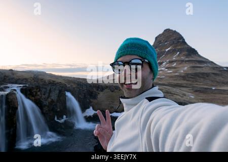 Jeune homme prenant des selfies aux cascades de Kirkjufell, Islande. Banque D'Images