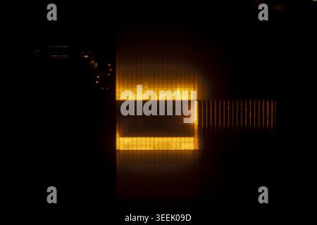 Vue aérienne d'un grand complexe de serres incandescentes la nuit avec des lumières orange vives éclairant la structure rectangulaire. Banque D'Images