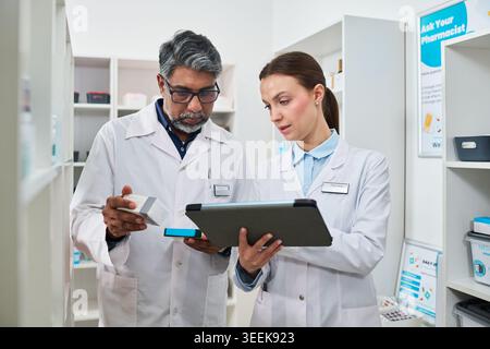 Pharmaciens indiens d'âge moyen examinant la boîte et le comprimé de médicaments en pharmacie, soutenant le flux de travail des ordonnances et le marketing des soins de santé Banque D'Images