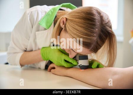 Femme focalisée examinant la peau au dermatoscope au cabinet médical Banque D'Images