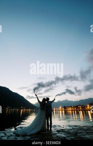 Couple heureux marqué par des lumières incandescentes embrassant sous le ciel crépusculaire avec panache de fumée Banque D'Images