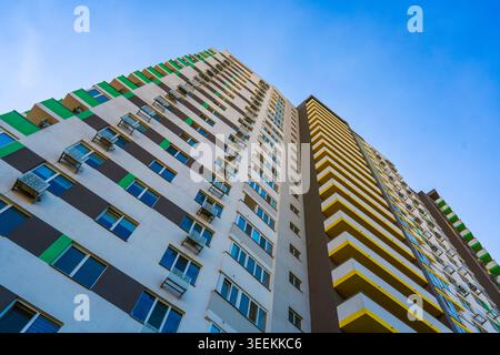 Immeuble résidentiel moderne de grande hauteur avec balcons verts et jaunes, fenêtres et climatiseurs sous ciel bleu clair. Développement immobilier Banque D'Images