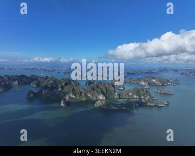 Une vue aérienne panoramique capture des îles karstiques spectaculaires émergeant d'eaux turquoises calmes sous un vaste ciel bleu clair avec des nuages blancs éparpillés Banque D'Images