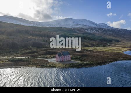 Vue aérienne de la maison rose sur la rive du Loch Glass avec des montagnes enneigées et un terrain accidenté à Dingwall, Écosse, Royaume-Uni. Banque D'Images