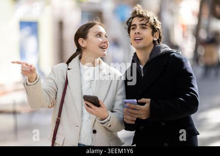 Jeune couple marchant dans la rue regardant les téléphones pour la carte de la ville Banque D'Images