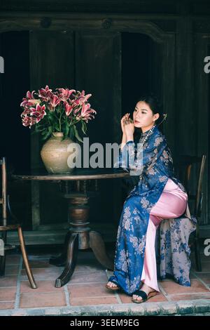 jeune femme dans floral ao dai assis près du vase de fleur. Nha Trang, Vietnam - 25 janvier 2026. Banque D'Images