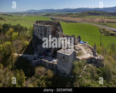 Vue aérienne des ruines médiévales du château de Likava sur une colline rocheuse entourée de champs verdoyants et de forêts avec un pont autoroutier en arrière-plan Lika Banque D'Images
