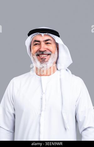 Homme arabe mature senior se présentant en kandora et ghutra émiratis traditionnels, souriant avec confiance, représentant la culture, l'identité et un positi Banque D'Images