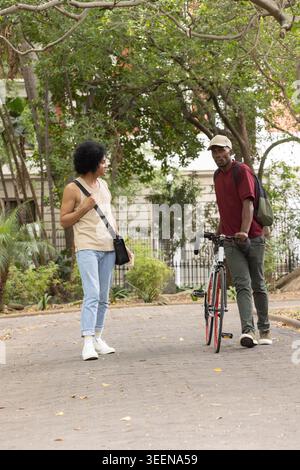 Hommes afro-américains discutant sur un chemin pavé avec des feuilles mortes, tenant un vélo de route avec des jantes rouges Banque D'Images
