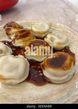 Des peljmeni traditionnels servis avec une sauce soja sucrée épicée et du sésame sur une assiette en céramique. Banque D'Images