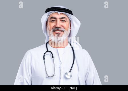 Homme arabe senior portant une kandora et un ghutra émiratis traditionnels, souriant avec confiance avec un stéthoscope autour du cou, incarnant la guérison professionnelle Banque D'Images