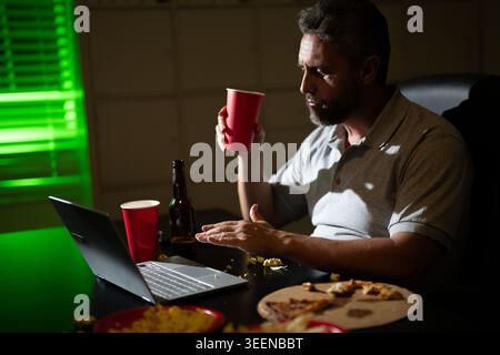 Homme d'affaires senior manger de la pizza en heures supplémentaires. Homme occupé mangeant le dîner et travaillant en ligne au bureau de nuit. Entrepreneur travaille tard dans la nuit tout en profitant d'un Banque D'Images