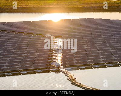 Vue aérienne de panneaux solaires reflétant la lumière dorée du soleil sur une surface calme du lac pendant le coucher du soleil Bensheim, Hesse, Allemagne. Banque D'Images