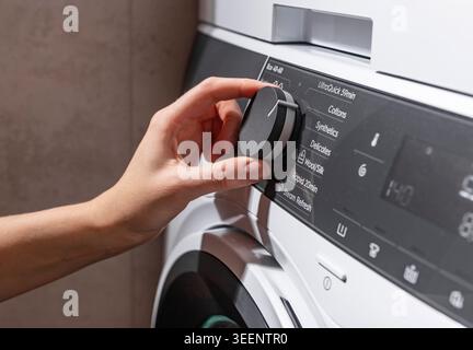Main tourner le bouton de commande sur un panneau de machine à laver moderne, sélectionner un programme de blanchisserie sur une interface d'appareil numérique, vue rapprochée de ménage Banque D'Images